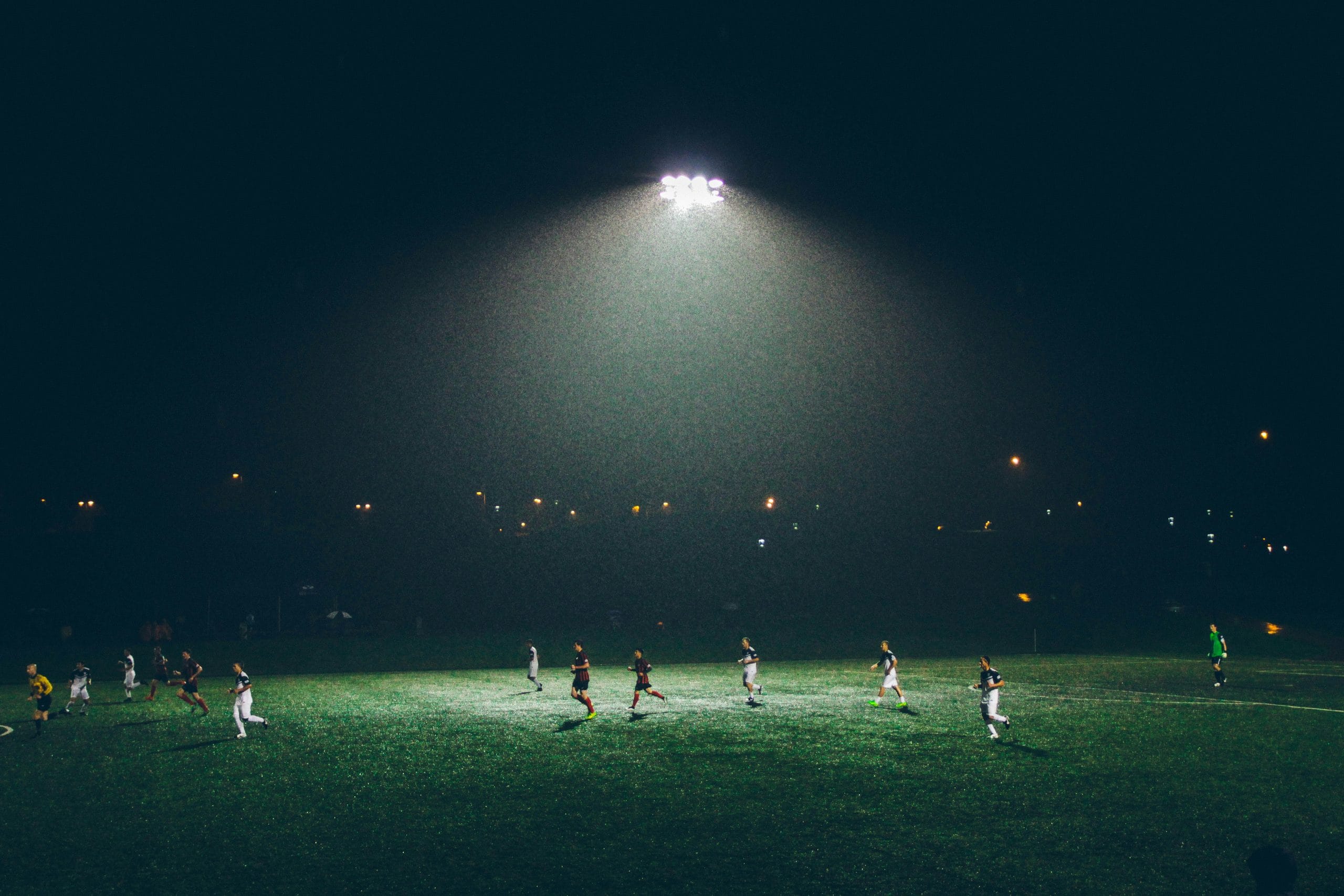 Partido de fútbol de noche en una cancha iluminada por un solo reflector